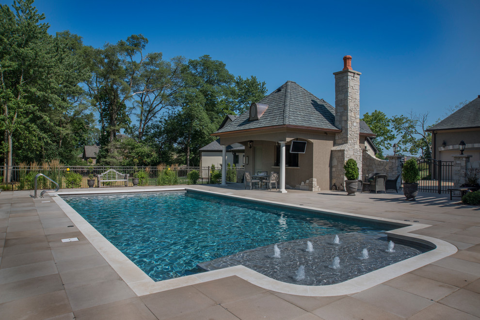 Modelo de piscina con fuente alargada tradicional de tamaño medio rectangular en patio trasero con adoquines de hormigón