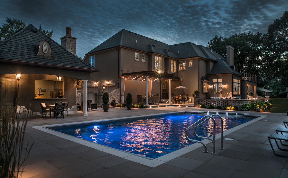 Modelo de piscina con fuente alargada tradicional de tamaño medio rectangular en patio trasero con adoquines de hormigón