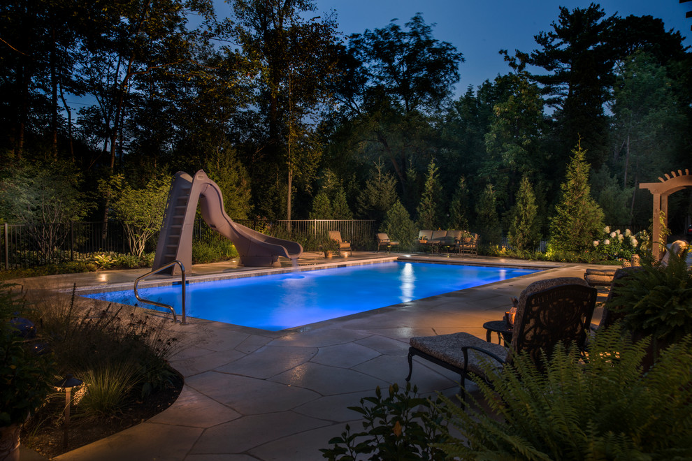 Foto de piscina con tobogán alargada rural de tamaño medio rectangular en patio trasero con adoquines de piedra natural