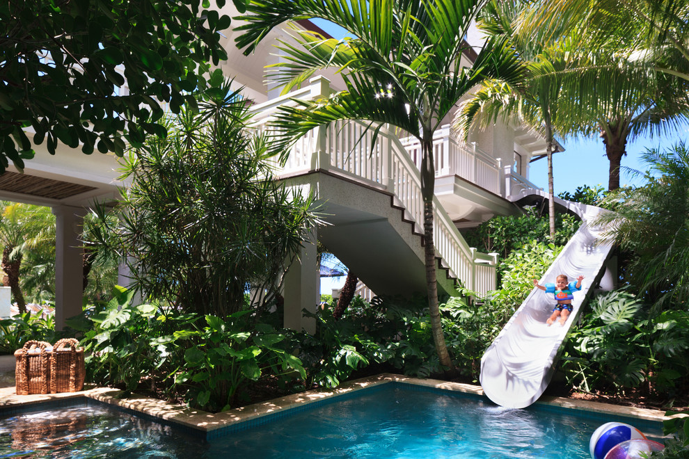 Esempio di un'ampia piscina a sfioro infinito tropicale personalizzata dietro casa con un acquascivolo e pavimentazioni in pietra naturale