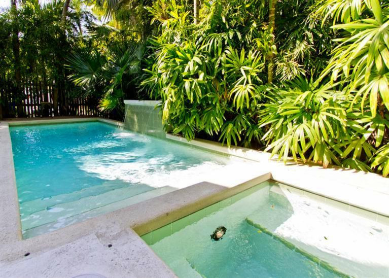 Modelo de piscinas y jacuzzis tropicales pequeños rectangulares en patio trasero con adoquines de piedra natural