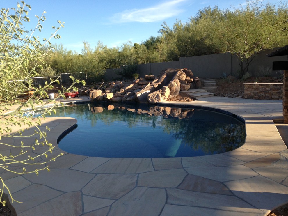 Medium sized back custom shaped lengths swimming pool in Phoenix with a water slide and natural stone paving.
