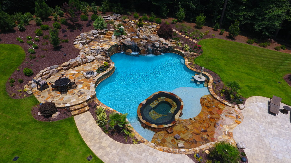 Diseño de piscinas y jacuzzis naturales rústicos grandes a medida en patio trasero con adoquines de hormigón