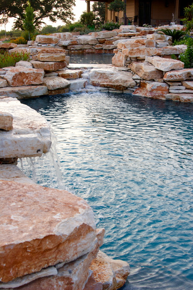 This is an example of an expansive rustic back custom shaped natural swimming pool in Dallas with a water feature and natural stone paving.