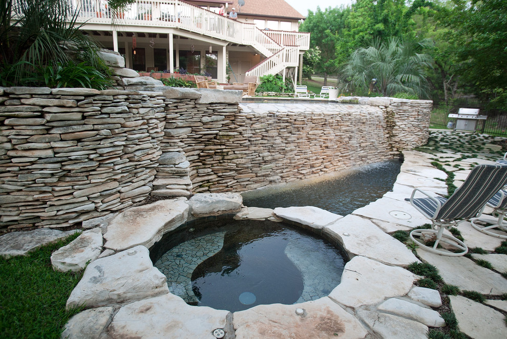 Foto di una grande piscina a sfioro infinito eclettica personalizzata dietro casa con una vasca idromassaggio e pavimentazioni in pietra naturale