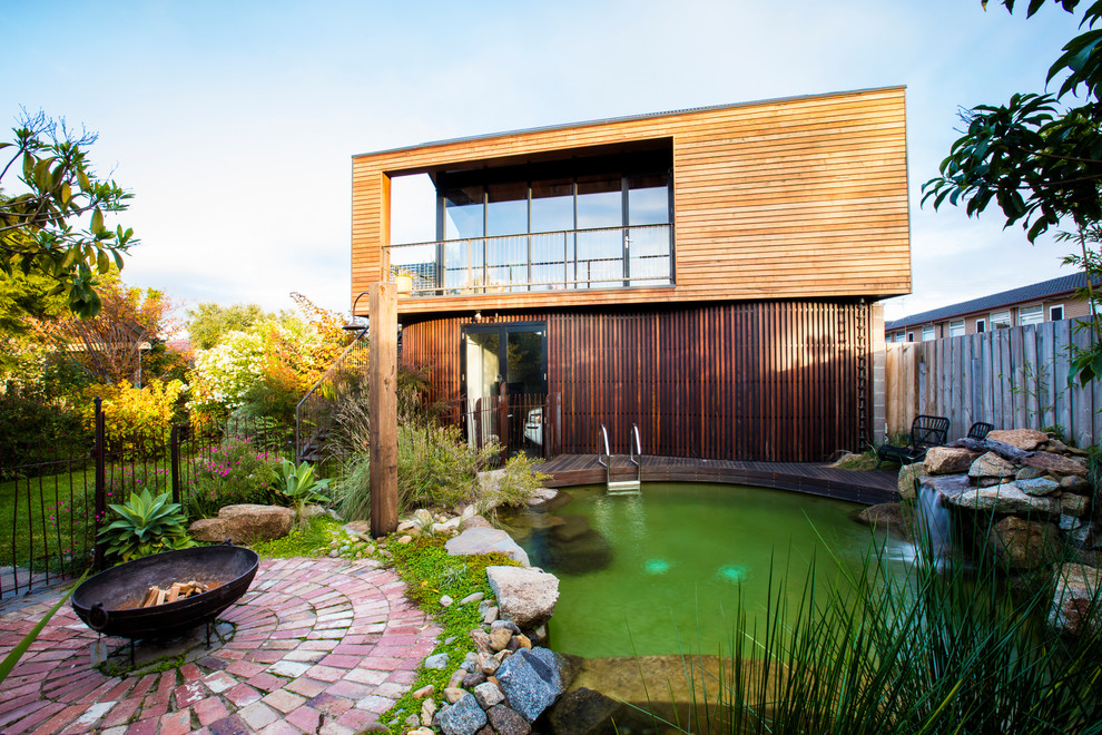 Стильный дизайн: естественный бассейн среднего размера, произвольной формы на заднем дворе с мощением клинкерной брусчаткой и перегородкой для приватности - последний тренд