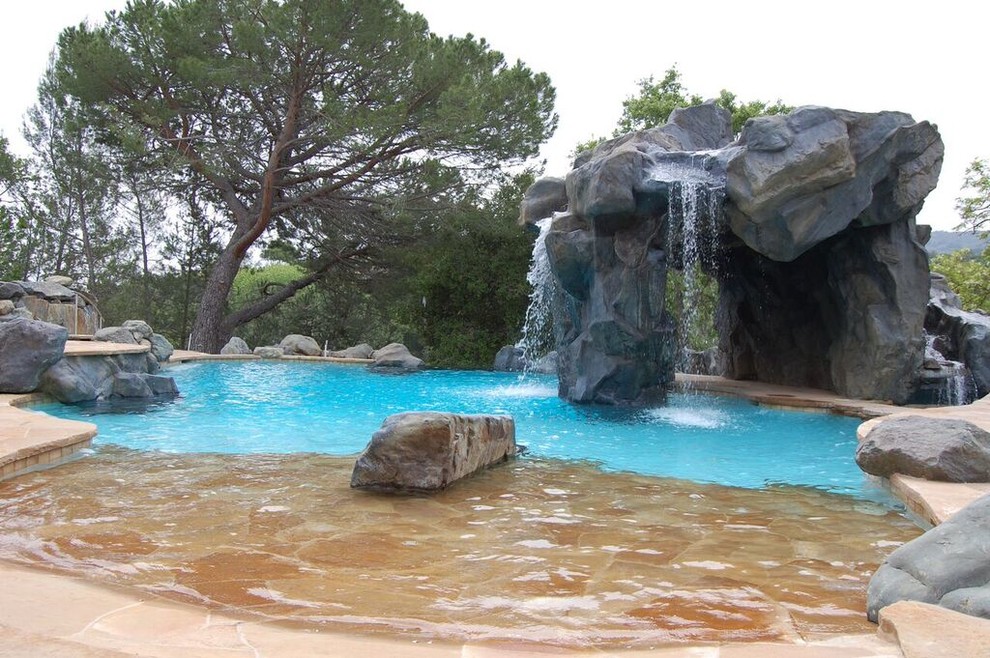 Cette image montre une grande piscine naturelle et arrière bohème sur mesure avec un point d'eau et des pavés en pierre naturelle.