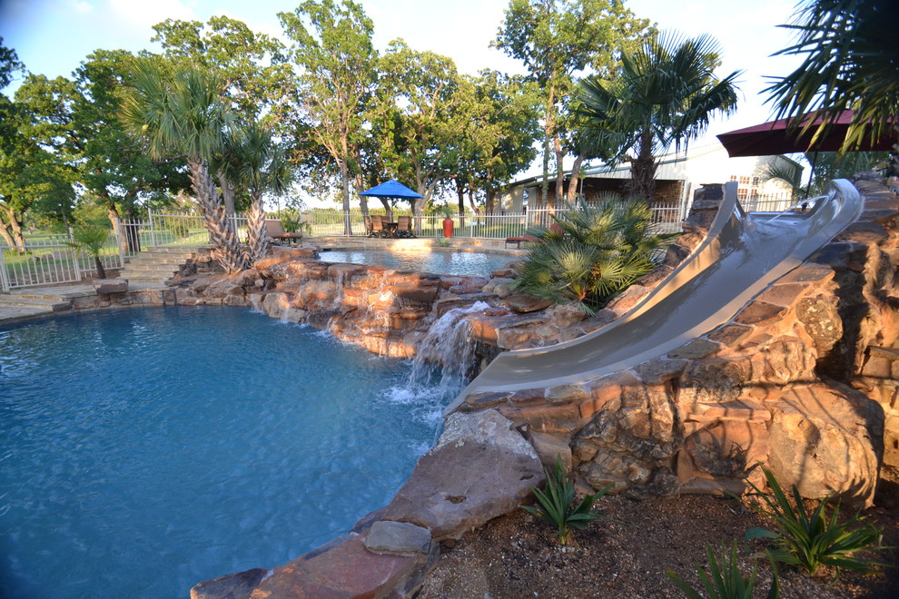 Imagen de piscina con tobogán tropical de tamaño medio a medida en patio trasero con adoquines de piedra natural
