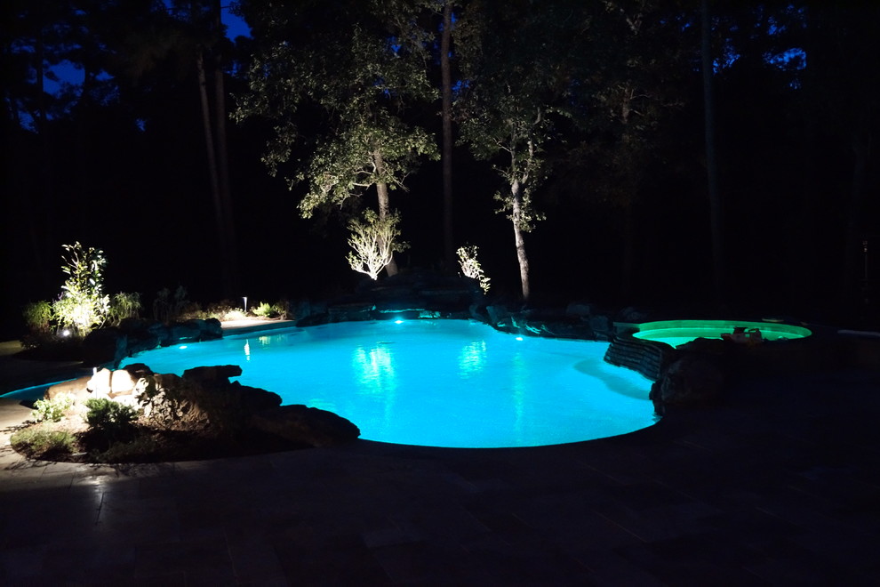 Diseño de piscina con fuente exótica grande a medida en patio trasero con adoquines de hormigón