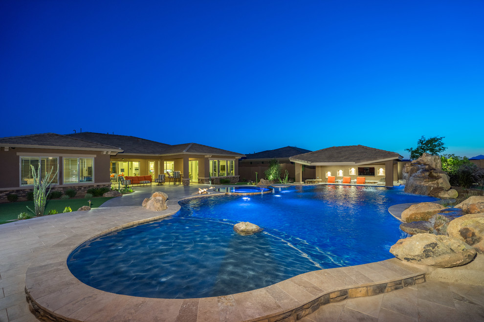 This is an example of a large classic back custom shaped swimming pool in Phoenix with natural stone paving.