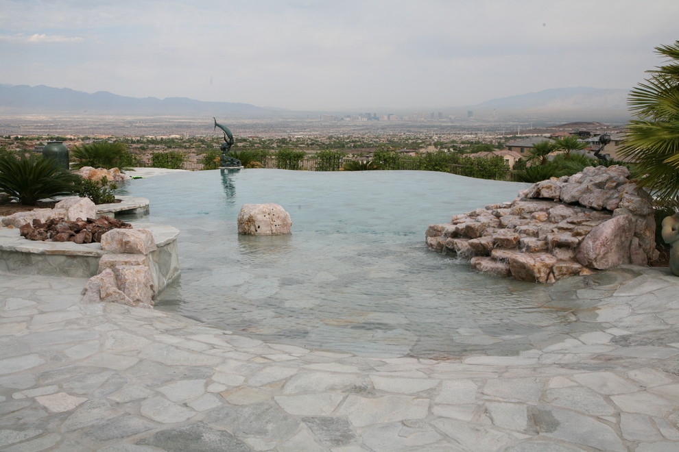 На фото: большой бассейн-инфинити произвольной формы на заднем дворе в морском стиле с фонтаном и покрытием из каменной брусчатки с