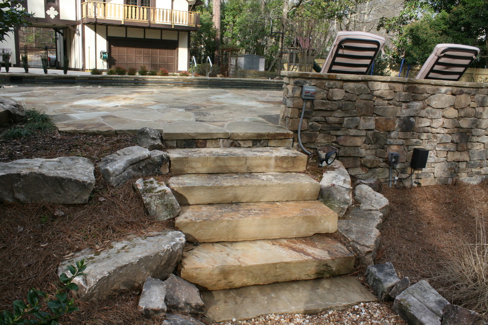 This is an example of a large rustic back rectangular natural swimming pool in Atlanta with a water feature and natural stone paving.