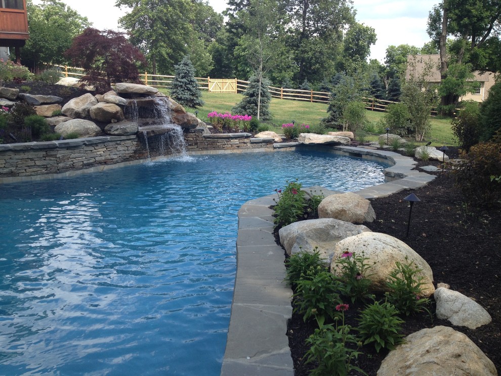Design ideas for a medium sized traditional back custom shaped lengths swimming pool in New York with a water feature and natural stone paving.