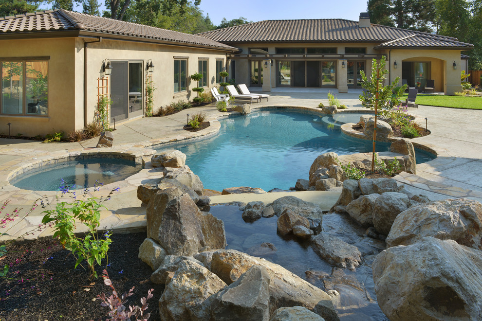 This is an example of an expansive mediterranean back custom shaped lengths swimming pool in San Francisco with a water feature and natural stone paving.