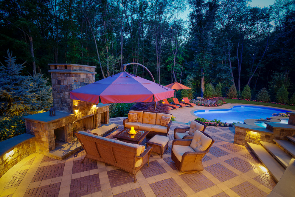 Diseño de piscinas y jacuzzis alargados actuales grandes tipo riñón en patio trasero con adoquines de hormigón