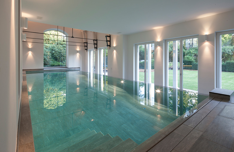 Réalisation d'une grande piscine intérieure design rectangle avec des pavés en pierre naturelle.