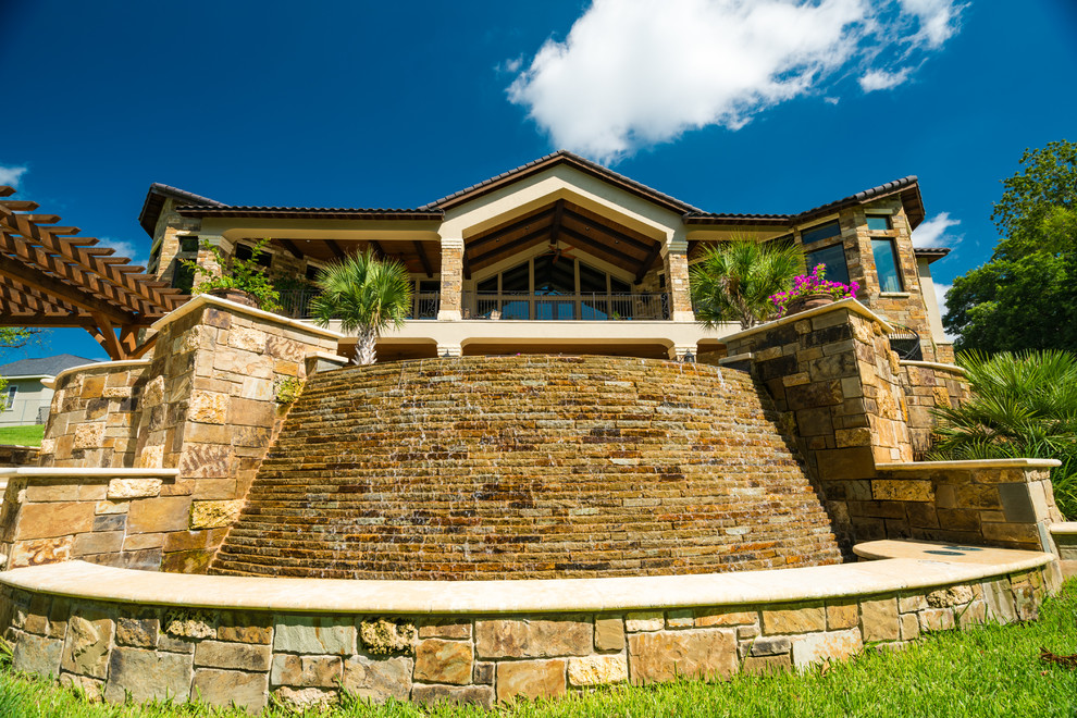 Exempel på en stor medelhavsstil anpassad infinitypool på baksidan av huset, med en fontän och naturstensplattor