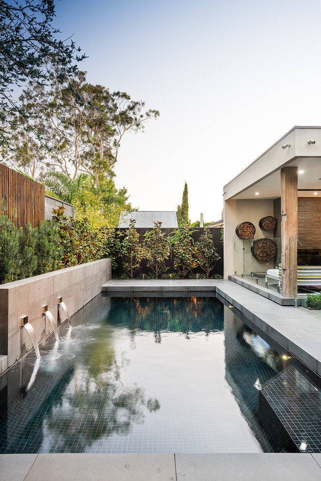 На фото: прямоугольный бассейн среднего размера на заднем дворе в современном стиле с фонтаном и покрытием из бетонных плит с
