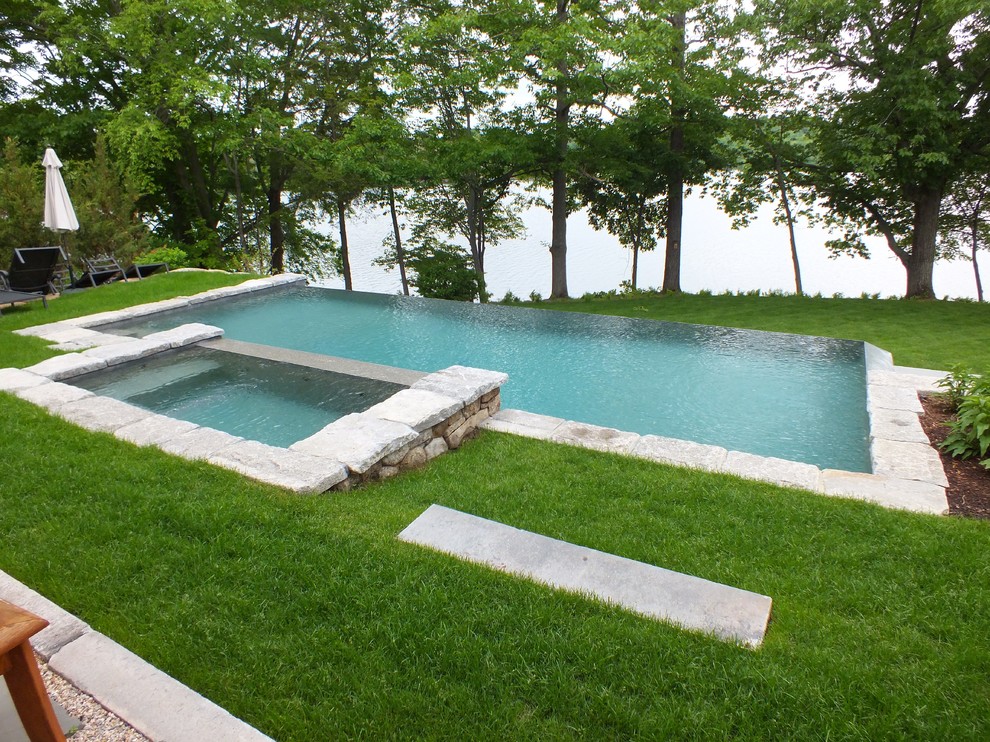 Esempio di una piscina a sfioro infinito chic rettangolare di medie dimensioni e dietro casa con una vasca idromassaggio e pavimentazioni in pietra naturale
