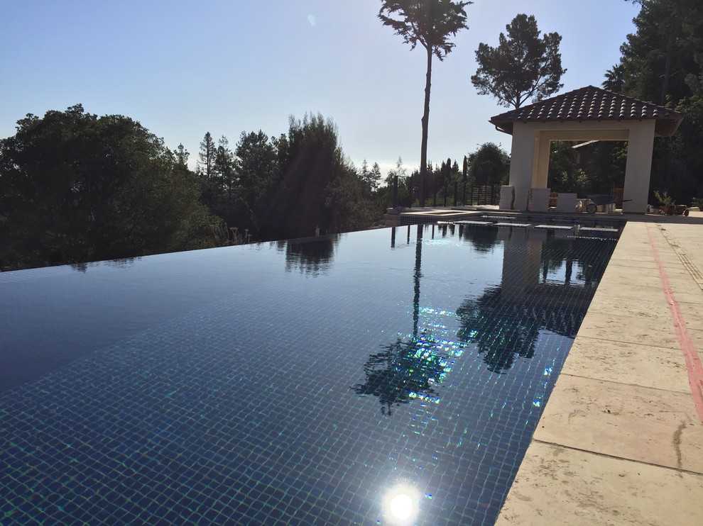 Esempio di una grande piscina a sfioro infinito contemporanea rettangolare dietro casa con pavimentazioni in pietra naturale