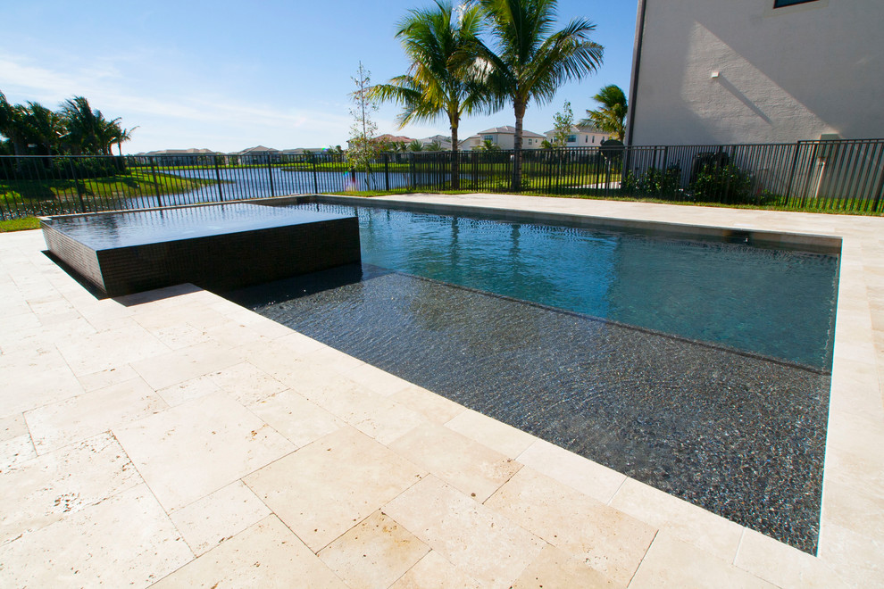 Réalisation d'une grande piscine arrière minimaliste rectangle avec un bain bouillonnant et des pavés en pierre naturelle.