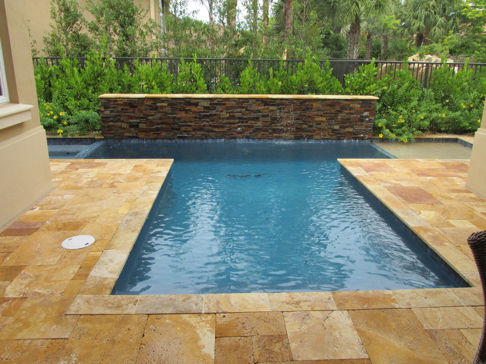 Réalisation d'une piscine à débordement et arrière minimaliste de taille moyenne et sur mesure avec un point d'eau et des pavés en pierre naturelle.