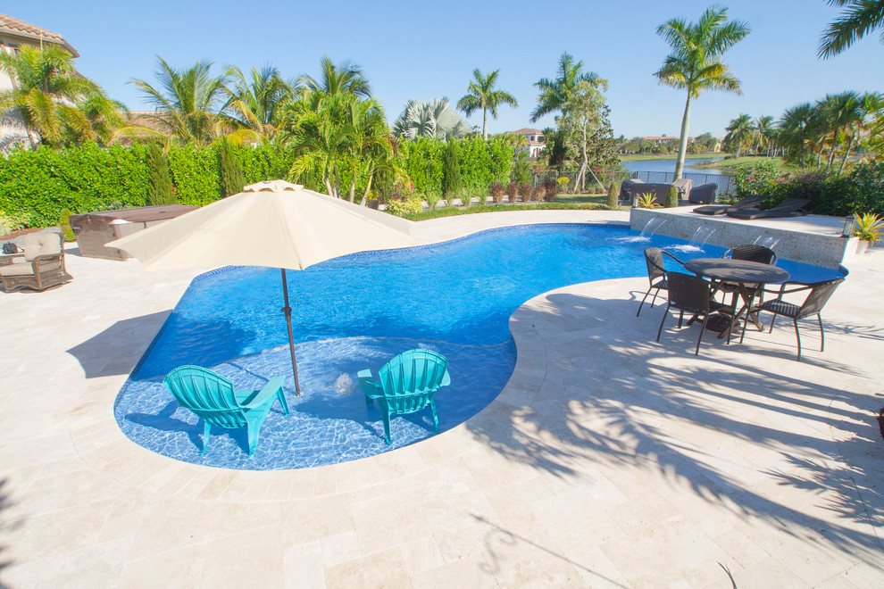 Example of a large beach style backyard stone and custom-shaped pool fountain design in Miami