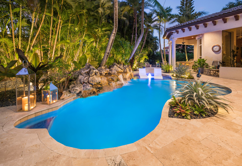 Ejemplo de piscina alargada tropical grande a medida en patio trasero con suelo de baldosas