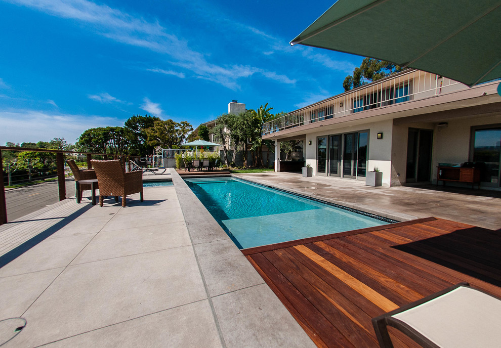 Diseño de piscina con fuente alargada moderna grande rectangular en patio trasero con losas de hormigón