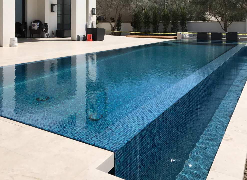 Modelo de piscinas y jacuzzis infinitos costeros grandes rectangulares en patio trasero con adoquines de piedra natural
