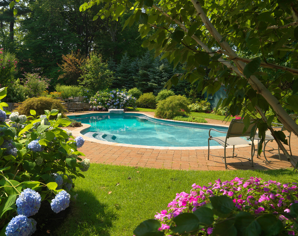 Immagine di una grande piscina classica a "C" dietro casa con pavimentazioni in mattoni e una vasca idromassaggio