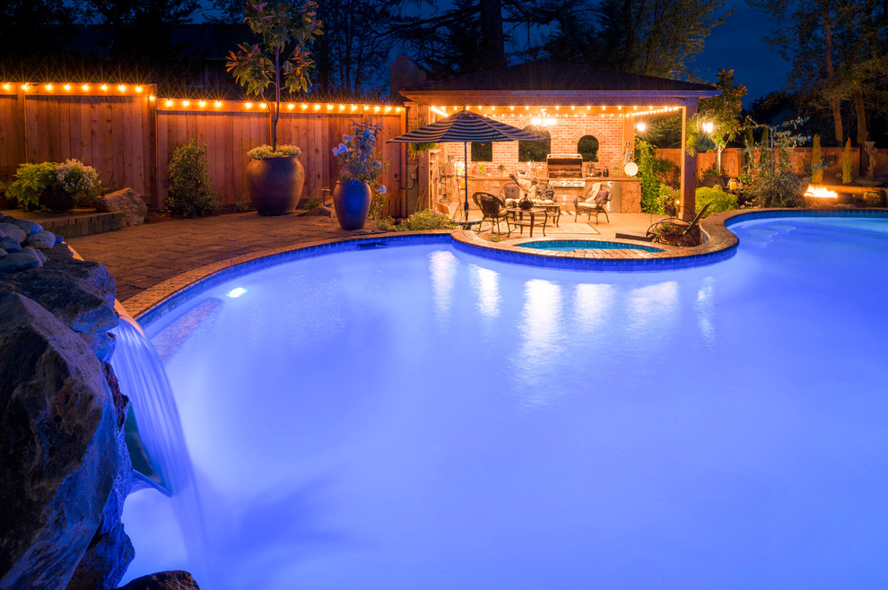 На фото: большой естественный бассейн в форме фасоли на заднем дворе в средиземноморском стиле с джакузи и мощением тротуарной плиткой