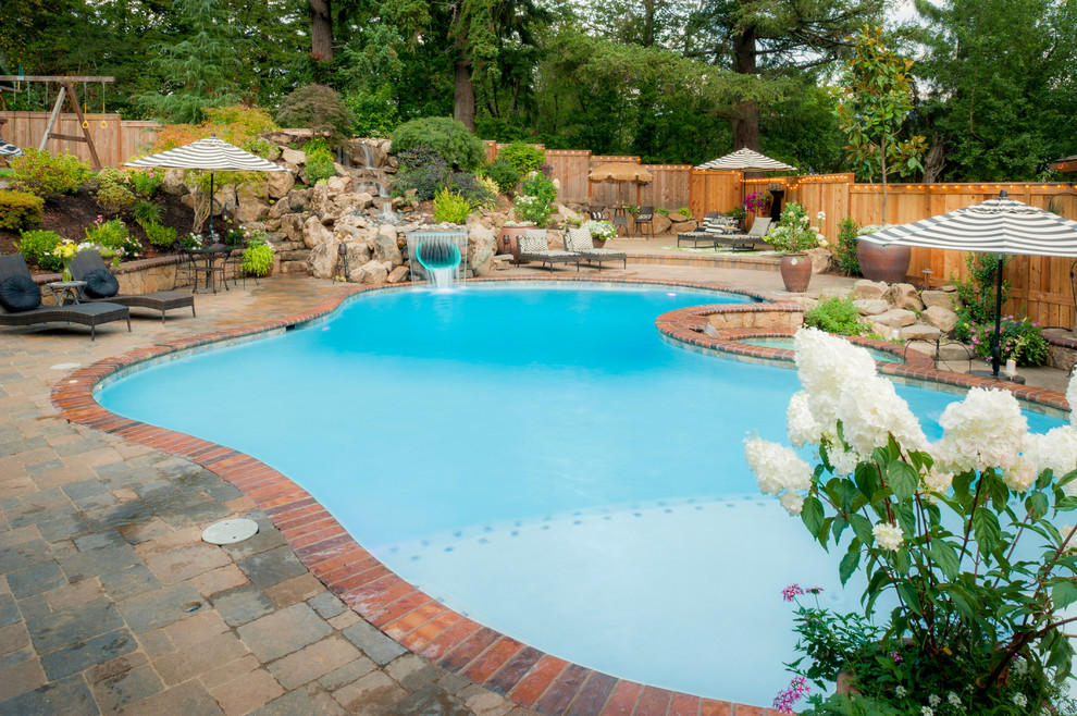 Photo of a large mediterranean back kidney-shaped infinity swimming pool in Portland with brick paving.