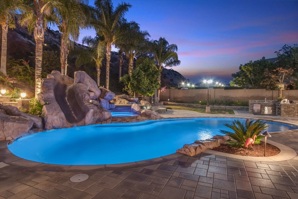 Example of a large island style backyard concrete paver and custom-shaped water slide design in Orange County
