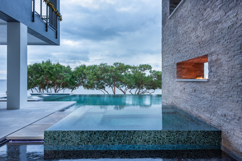Cette image montre une piscine à débordement et arrière minimaliste de taille moyenne et sur mesure avec un bain bouillonnant et des pavés en béton.