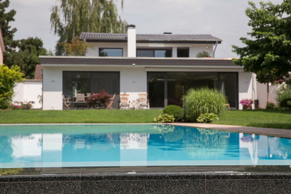 Modelo de piscina infinita clásica grande rectangular en patio lateral con adoquines de piedra natural