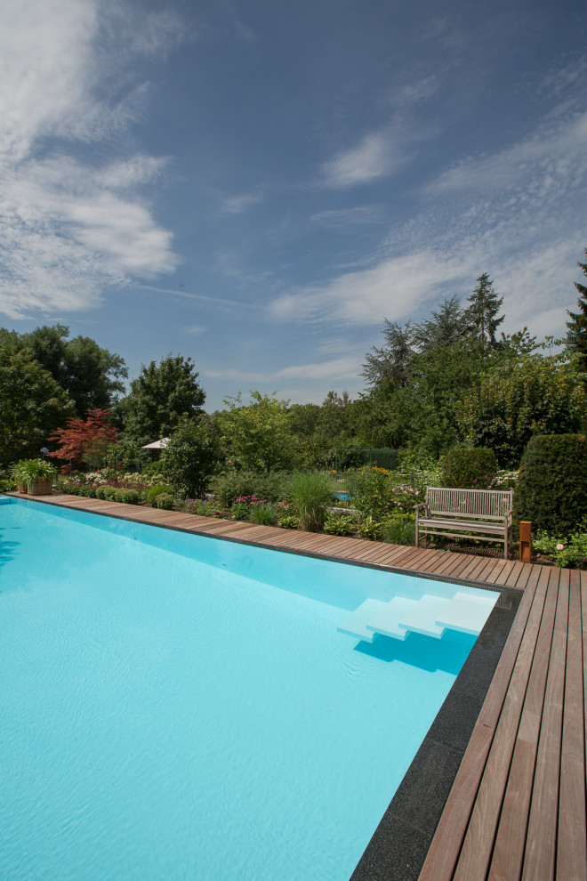 Immagine di una grande piscina a sfioro infinito tradizionale rettangolare nel cortile laterale con pavimentazioni in pietra naturale