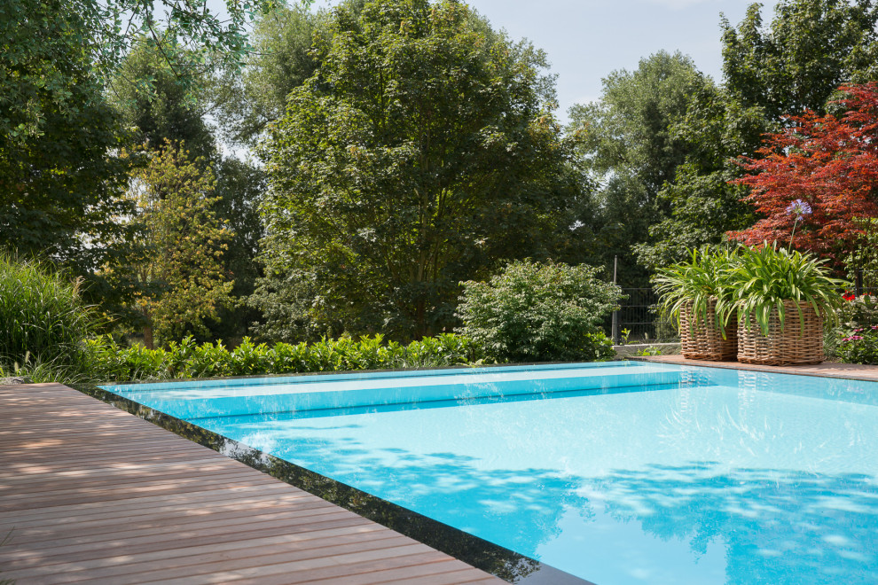Large traditional side rectangular infinity swimming pool in Frankfurt with natural stone paving.