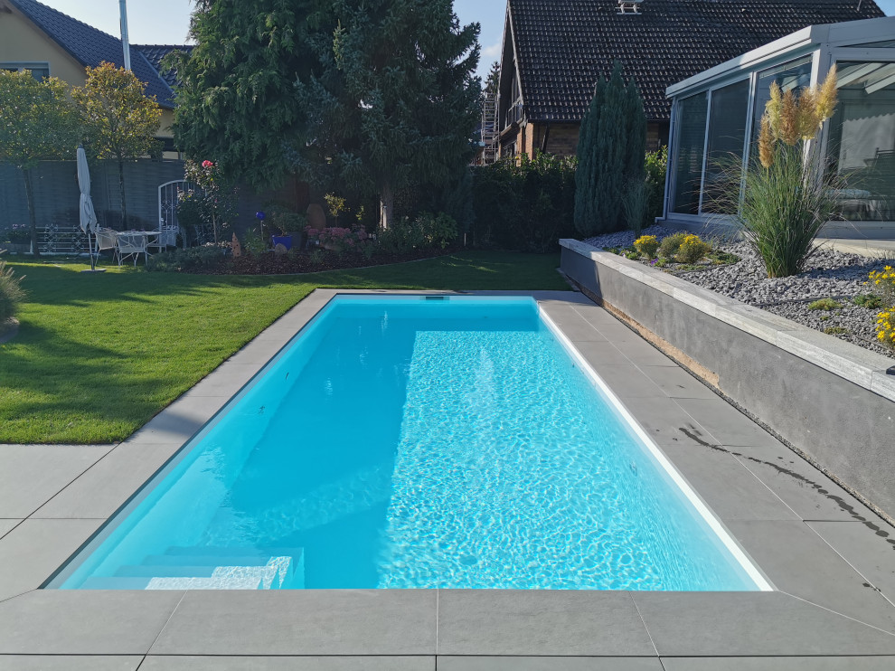 Modelo de piscina contemporánea de tamaño medio rectangular en patio lateral con suelo de baldosas