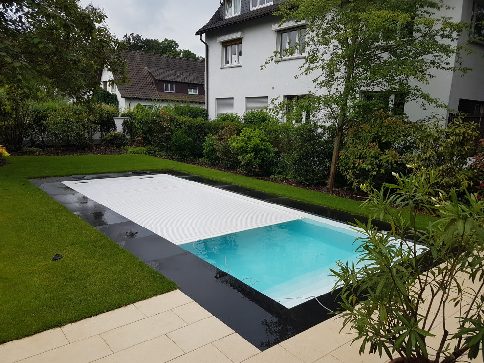 Modelo de piscina clásica grande rectangular en patio delantero con adoquines de piedra natural