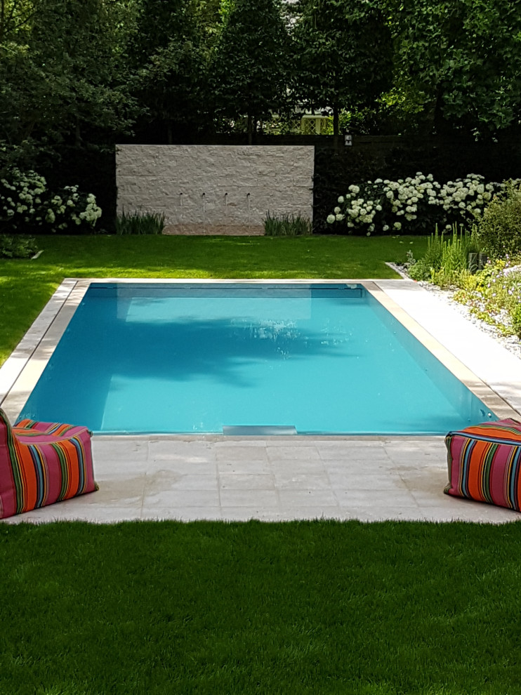 Large contemporary side rectangular infinity swimming pool in Frankfurt with natural stone paving.