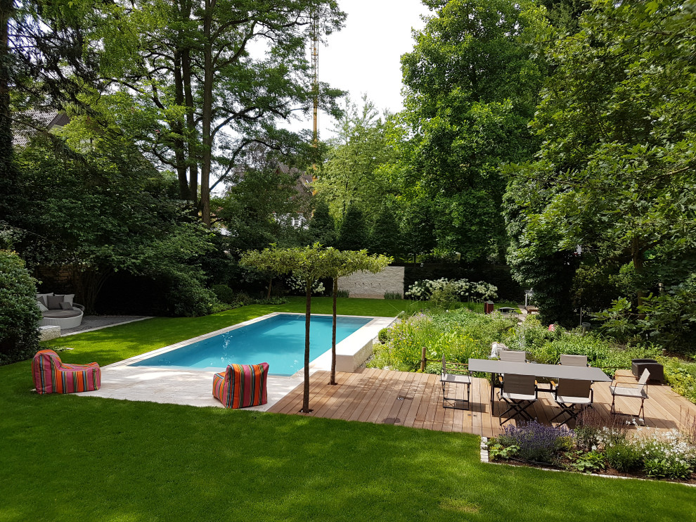 Modern inredning av en stor rektangulär pool längs med huset, med vattenrutschkana och naturstensplattor