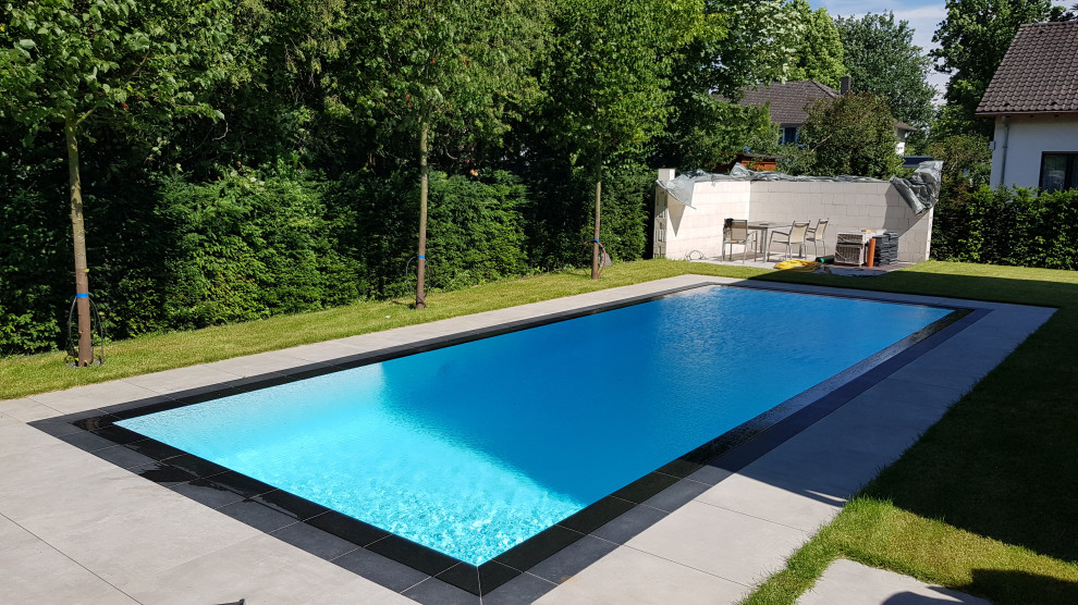 Стильный дизайн: большой прямоугольный бассейн-инфинити на боковом дворе в современном стиле с покрытием из каменной брусчатки - последний тренд