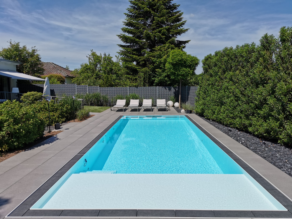 Diseño de piscina infinita contemporánea grande rectangular en patio lateral con suelo de baldosas