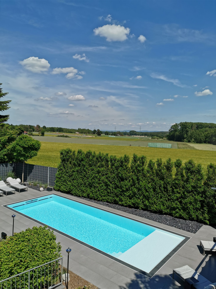 Modelo de piscina infinita contemporánea grande rectangular en patio lateral con suelo de baldosas