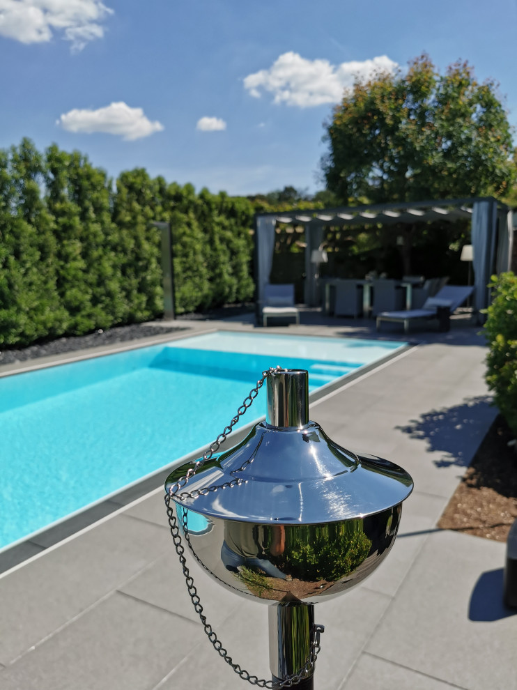 Modelo de piscina infinita actual grande rectangular en patio lateral con suelo de baldosas