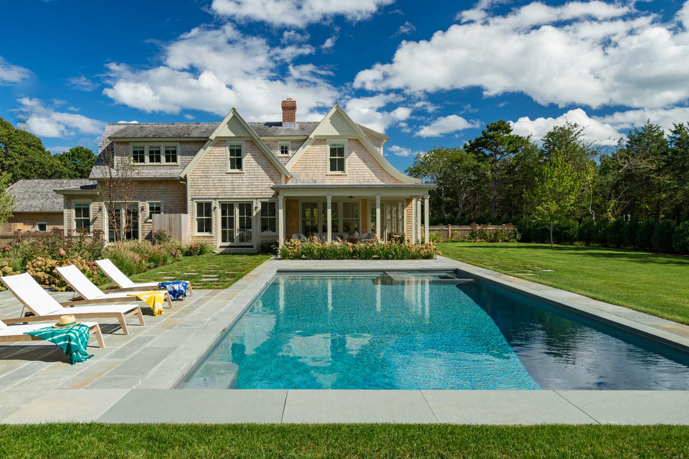 Modelo de piscina alargada costera grande rectangular en patio trasero con adoquines de piedra natural