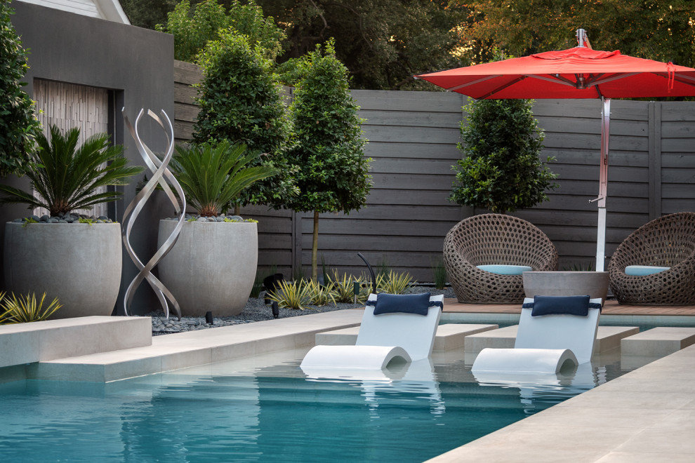 На фото: большой прямоугольный ландшафтный бассейн на заднем дворе в стиле модернизм с покрытием из каменной брусчатки с