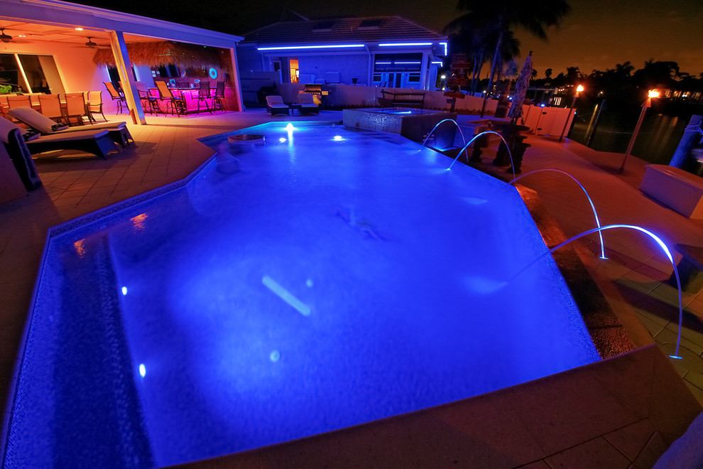 Réalisation d'une piscine à débordement et arrière minimaliste de taille moyenne et sur mesure avec un point d'eau et des pavés en béton.