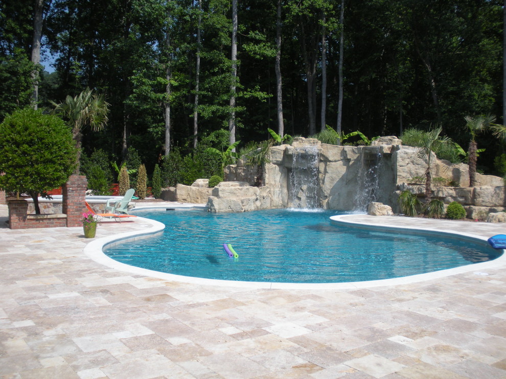 Réalisation d'une grande piscine arrière tradition sur mesure avec un point d'eau, un bain bouillonnant et des pavés en pierre naturelle.